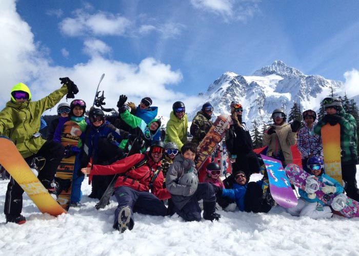 SOS Outreach youth posing in front of a mountain with skis and snowboards